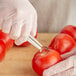 A person in gloves using a Vollrath Redco Tomato King Scooper to core a tomato at a salad bar.