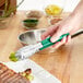 A person using a Choice green and silver stainless steel scalloped tong to serve green food.