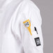 A person wearing a white Chef Revival short sleeve chef coat with a yellow device in the pocket.