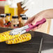 A person using Choice purple stainless steel scalloped tongs to grill corn on the cob.