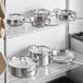A metal rack with Vigor stainless steel pots and pans on it.