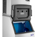A Manitowoc air cooled ice machine with blue and white accents and a rectangular black object with holes on top.