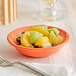 An Acopa Capri Valencia Orange stoneware fruit bowl on a table with a bowl of fruit.