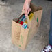 A person holding a Duro brown paper shopping bag with food in it.