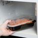 A hand placing a Pactiv Newspring plastic container of food in a microwave.