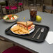 A black Carlisle fast food tray with a sandwich and chips on it.