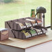 A brown 2-tier self-serve organizer set with bins on a counter with coffee cups and sugar.