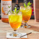 A glass of Monin Premium Honey Jasmine flavored liquid with ice and mint leaves.