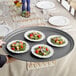 A person holding a Choice gray oval non-skid serving tray with salads.