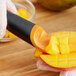 A person using a black and orange OXO Good Grips mango slicer to cut a mango.