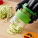 A person using an OXO hand-held spiralizer to cut zucchini into noodles.