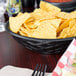 A black round weave basket filled with chips on a table.