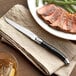 An Acopa stainless steel steak knife on a plate with steak and green beans.