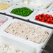 A row of white Cambro food pans filled with a variety of food on a counter.
