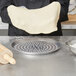 A person holding a piece of dough over a American Metalcraft Super Perforated Pizza Pan with a rolling pin.