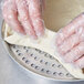 A person wearing plastic gloves using an American Metalcraft Super Perforated Pizza Pan to make dough.