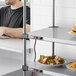 A man in a black shirt behind a Metro stainless steel heated shelf with plates of sandwiches and french fries on it.