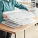 A person holding a Baker's Mark polypropylene tray cover over trays of cookies.