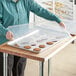 A woman using a Choice full size polypropylene bun and sheet pan cover to display cookies on a table.