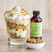 A dessert in a glass with a bowl of nuts and a bottle of LorAnn Oils Pistachio Bakery Emulsion.