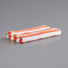 A folded coral red and white striped Monarch Brands pool towel.