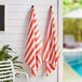 Two Monarch Brands coral red striped pool towels hanging on white hooks.