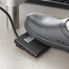 A black shoe using a black foot pedal to weigh food on a black Tor Rey portion scale.