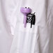 A white Chef Revival long sleeve chef coat with black piping and a purple object in the pocket.
