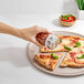 A hand using an OXO Good Grips glass shaker with a stainless steel top to sprinkle pepper over a pizza.
