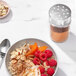A bowl of oatmeal with fruit and nuts next to an OXO Good Grips spice shaker.