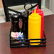 A black rectangular wrought iron condiment caddy with condiments and sugar packets on a table.