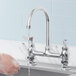 A Waterloo deck-mount faucet with running water over hands.