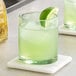 Two Acopa Pangea green rocks glasses filled with limeade and garnished with lime wedges on a table.