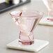 Two mauve Acopa Pangea martini glasses with liquid on a marble counter.