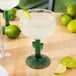 A Libbey cactus margarita glass with a drink on a table with lime wedges.