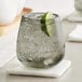 A Acopa Pangea stemless wine glass with ice and a lime wedge on a table.