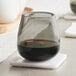 An Acopa gray stemless wine glass filled with dark liquid sits on a coaster on a table.