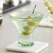 An Acopa Pangea green martini glass filled with a green drink and olives on a table.