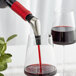 A Vacu Vin wine pourer attached to a bottle pouring red wine into a glass.