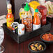 A HS Inc. charcoal polyethylene condiment organizer on a table with bowls of salsa, hot sauce, and ketchup.