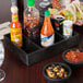 A black HS Inc. condiment organizer with various food items on a table.