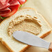 A knife spreading French's Stone Ground Dijon Mustard on a piece of bread.