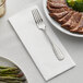 A Hoffmaster white linen-like napkin with a fork and plate of meat and vegetables.