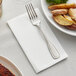 A Hoffmaster White Linen-Like dinner napkin with a fork on a plate of food.