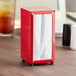 A red Choice tabletop napkin dispenser with white napkins on a table.