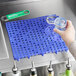 A person pouring a liquid into a blue Choice interlocking bar mat on a counter.