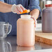 A man in gloves pouring liquid from a measuring cup into a Choice gallon container with an orange cap.