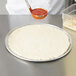A person putting pizza dough on an American Metalcraft wide rim pizza pan.