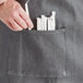 A person's hand putting a stick in the pocket of a gray denim bistro apron.
