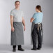 A man and woman wearing Acopa Kennett grey denim bistro aprons with natural webbing.